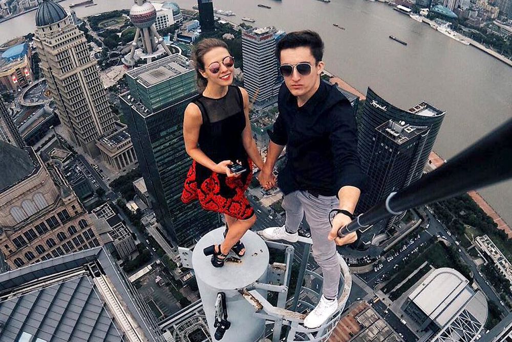 Dos jóvenes haciéndose un selfie sobre una plataforma adosada a un rascacielos.
