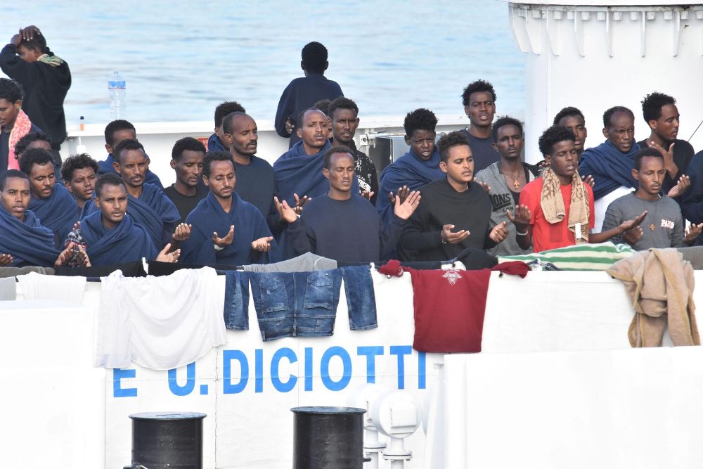 Migrantes rezan a la espera del desembarco del barco italiano de la Guardia Costera en Catania.