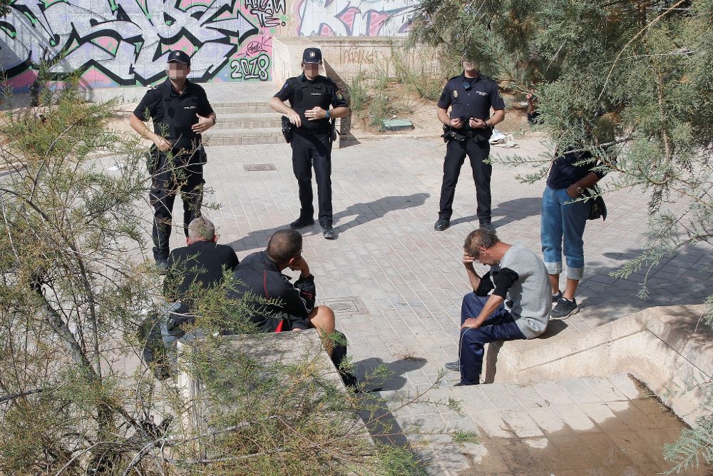 Agentes de policía custodian a los cuatro indigentes, en calidad de testigos, que compartían lugar de pernoctación con otro indigente que ha sido hallado muerto en Alicante.
