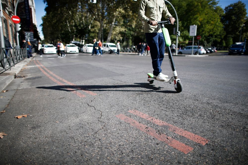 Un patinete pasa cerca de una línea naranja que indica restricción al tráfico en el centro de Madrid.