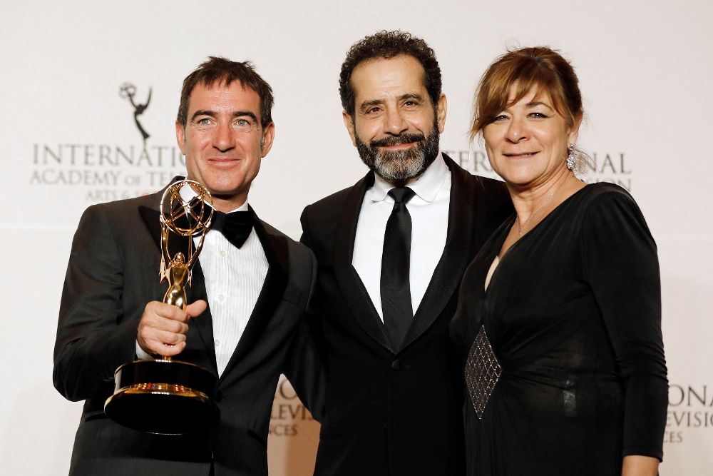 El actor estadounidense Tony Shalhoub (c) posa junto al guionista español Alex Pina (i) y la productora ejecutiva Sonia Martínez (d) mientras sostienen su premio a Mejor Serie Dramática por "La casa de papel".