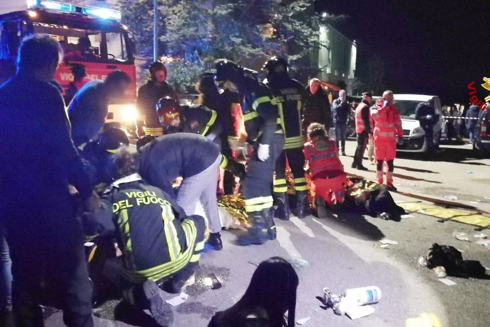 Los bomberos y persona de emergencias atienden a las víctimas de la estampida sobre el suelo de la calle a la puerta de la discoteca de Corinaldo.