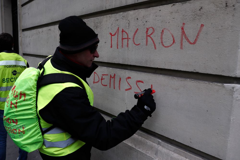 Un chaleco amarillo escribe "Macron dimisión" en una pared durante las protestas de estods días en París.