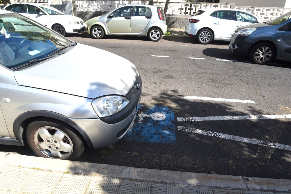 Un vehículo no autorizado ocupando la mitad de una plaza de aparcamiento destinada a personas con discapacidad.