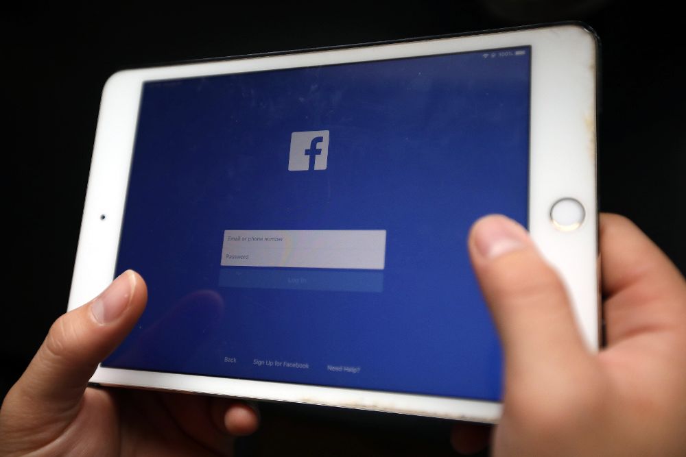 Una persona sostiene un dispositivo electrónico en la que aparece la página de inicio de la red social Facebook.
