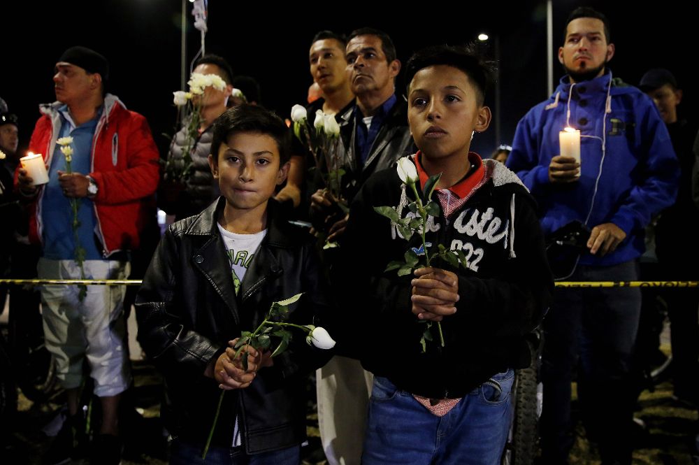 Dos niños sostienen rosas blancas durante un plantón este jueves frente a la Escuela de Cadetes de Policía General Francisco de Paula Santander, en Bogotá.Leonardo Muñoz (EFE)