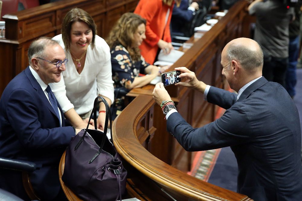 El diputado del PP José Estadella (d) fotografía a la diputada de Nueva Canarias, Gladis Acuña, con el consejero de Sanidad del Gobierno de Canarias, José Manuel Baltar, antes de comenzar la sesión plenaria.